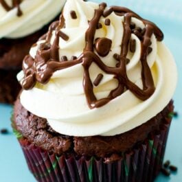 chocolate cupcakes topped with white chocolate frosting and chocolate sprinkles on a blue plate