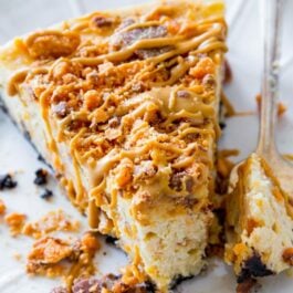 slice of peanut butter Butterfinger cheesecake on a white plate with a fork