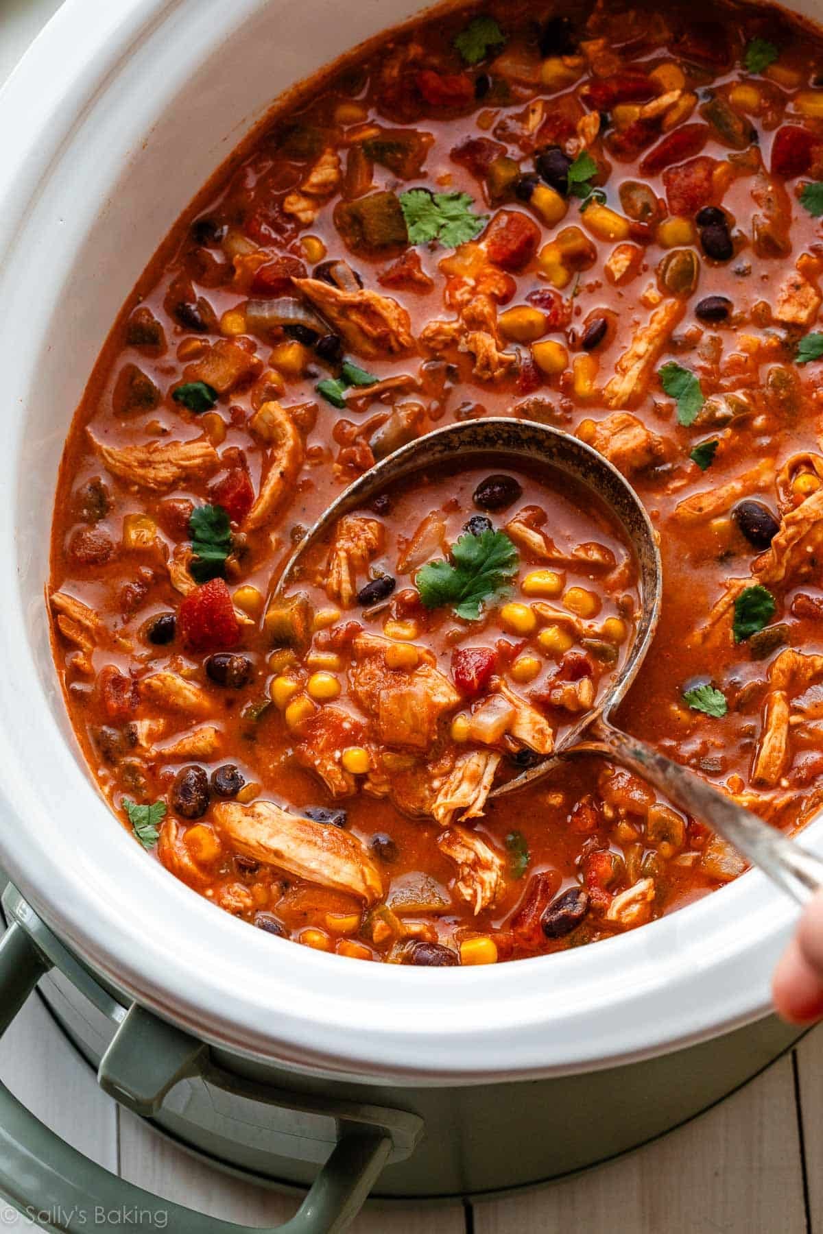 ladle in slow cooker of chicken chili with fresh chopped cilantro on top.