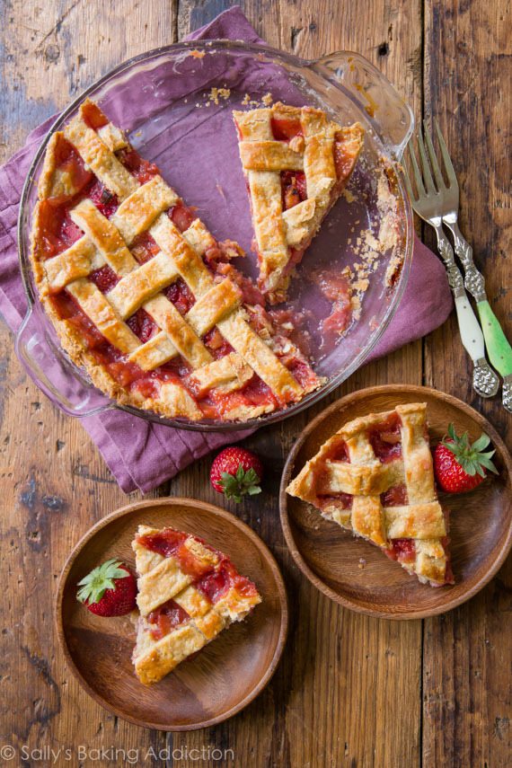 overhead image of strawberry rhubarb pie in a glass pie dish and slices of pie on wood plates