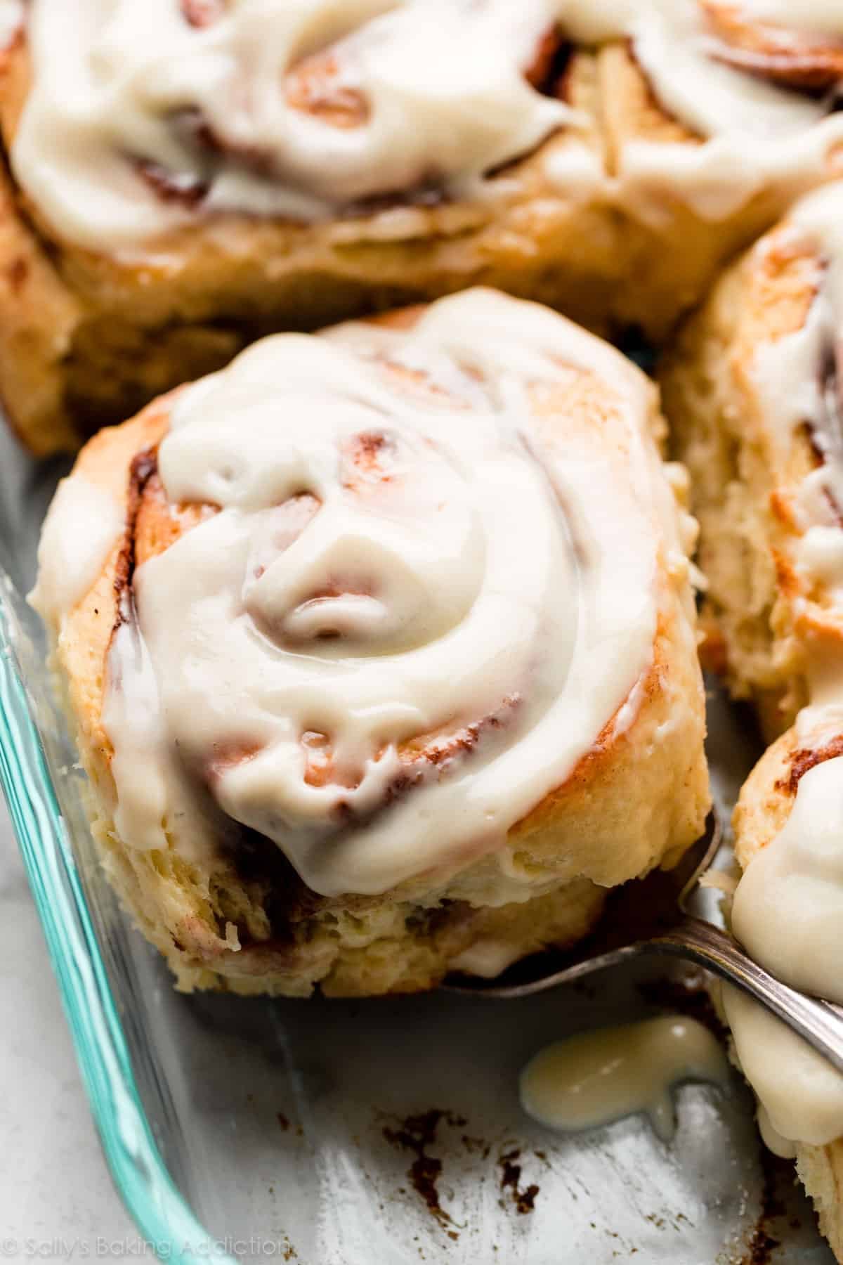 big cinnamon roll with cream cheese icing pictured in a glass baking dish