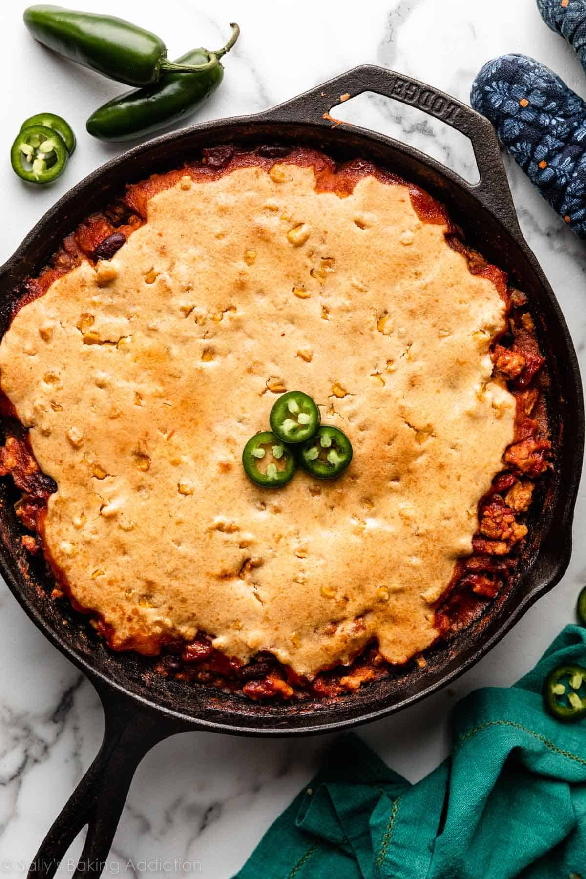 chili in a black cast iron skillet topped with cornbread and sliced jalapeños.