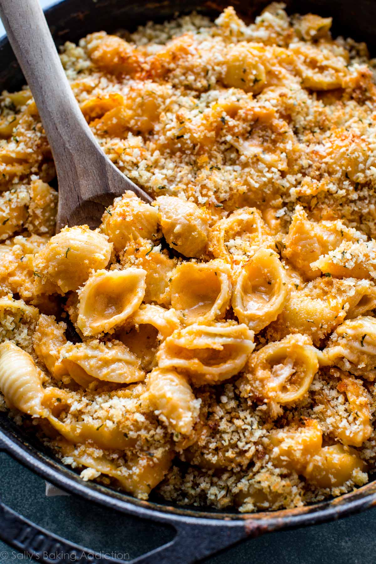 baked macaroni and cheese in a cast iron skillet with a wood spoon