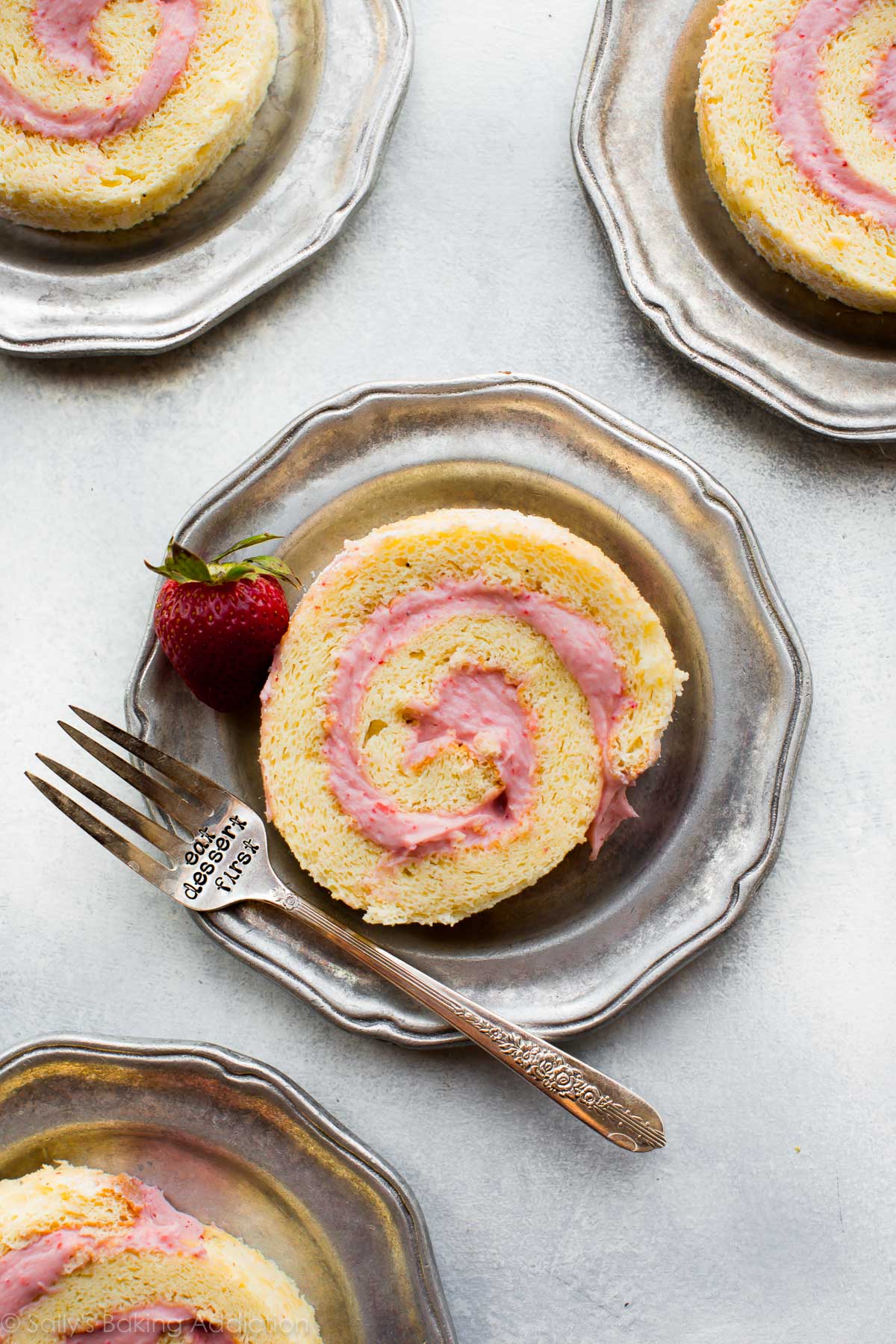 slices of strawberries and cream cake roll on silver plates with a fork