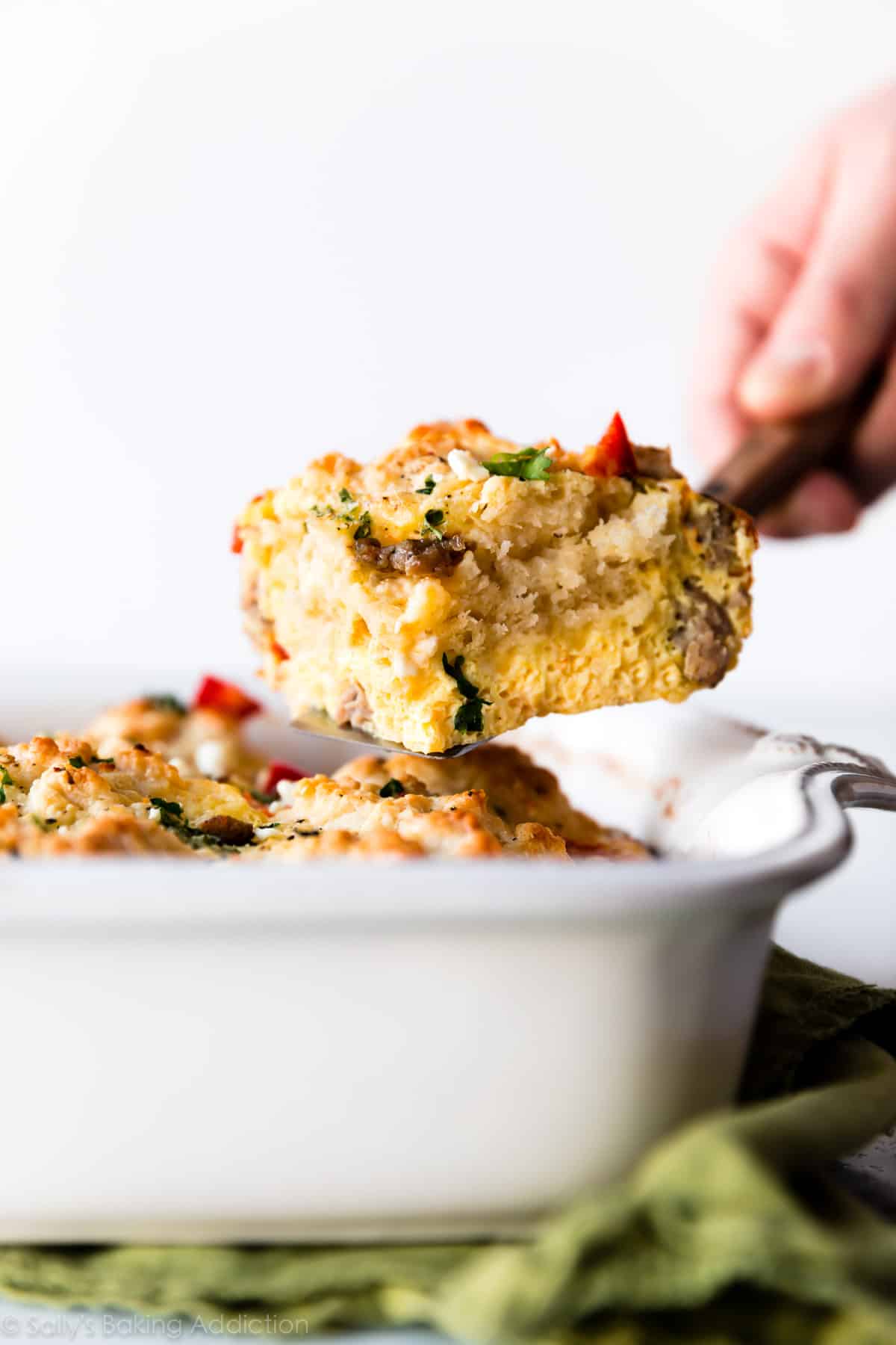 a slice of biscuit breakfast casserole on a server being removed from a baking dish