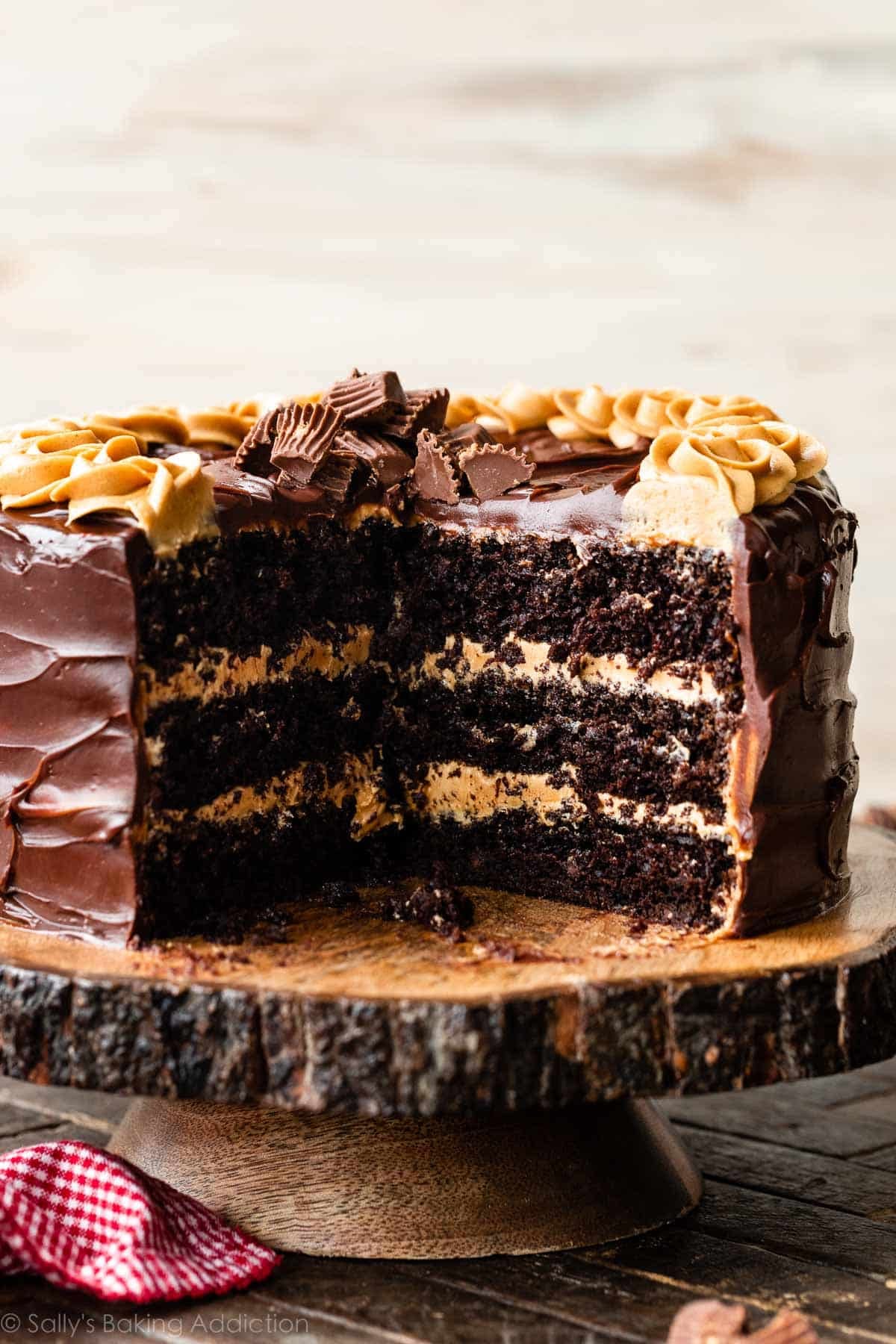 3 layer chocolate cake with peanut butter frosting and dark chocolate ganache on wood cake stand.