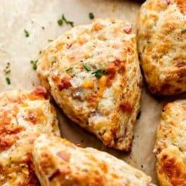 ham and cheddar cheese scones with chives and sea salt garnish on top sitting on brown parchment paper.
