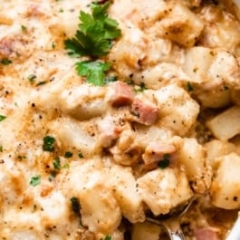 cheesy ham and potato casserole in white dish with serving spoon sitting in it.