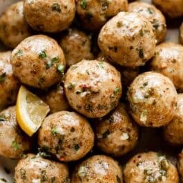 chicken meatballs in a pile topped with lemon butter herb sauce with red pepper flakes.
