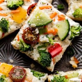 veggie pizza with fresh broccoli, red pepper, cucumber, cherry tomatoes, parmesan cheese, and scallion on top.