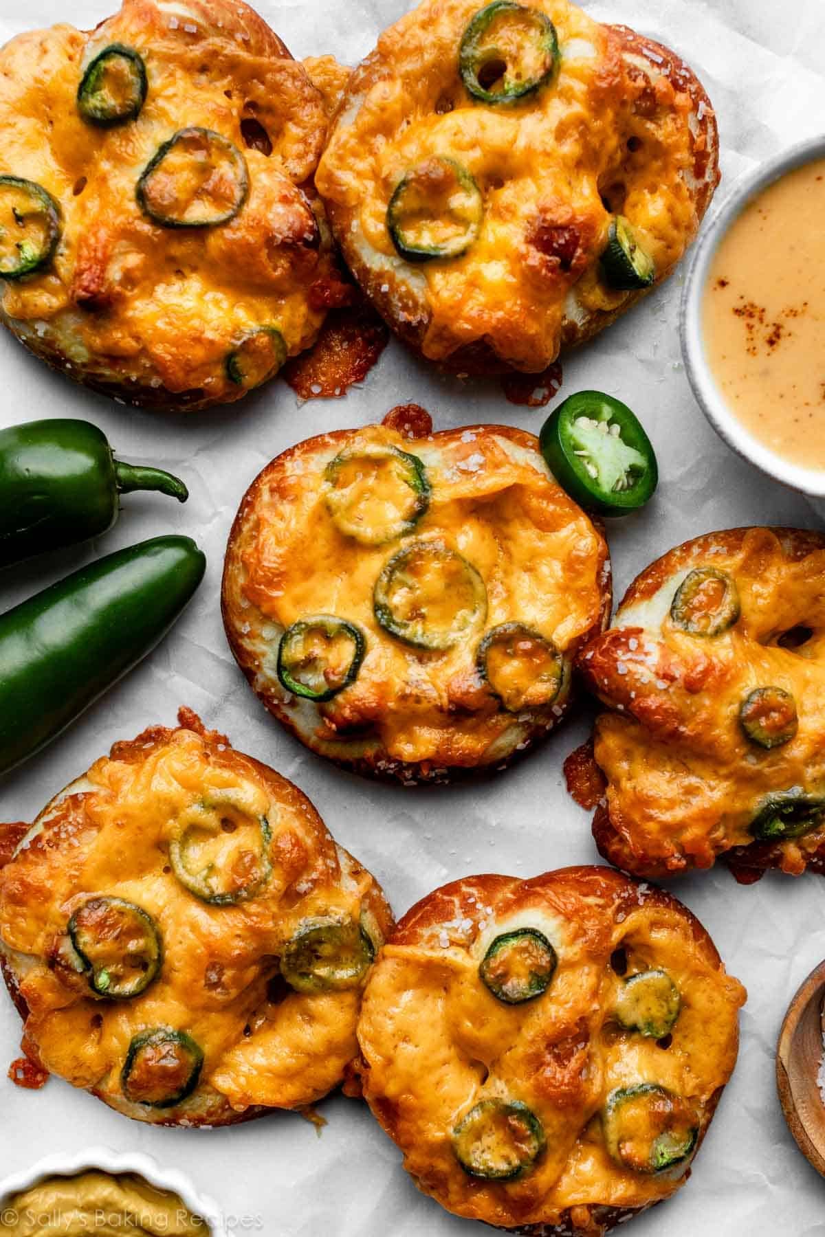 homemade soft pretzels topped with jalapeño slices and melted cheese arranged on parchment paper.