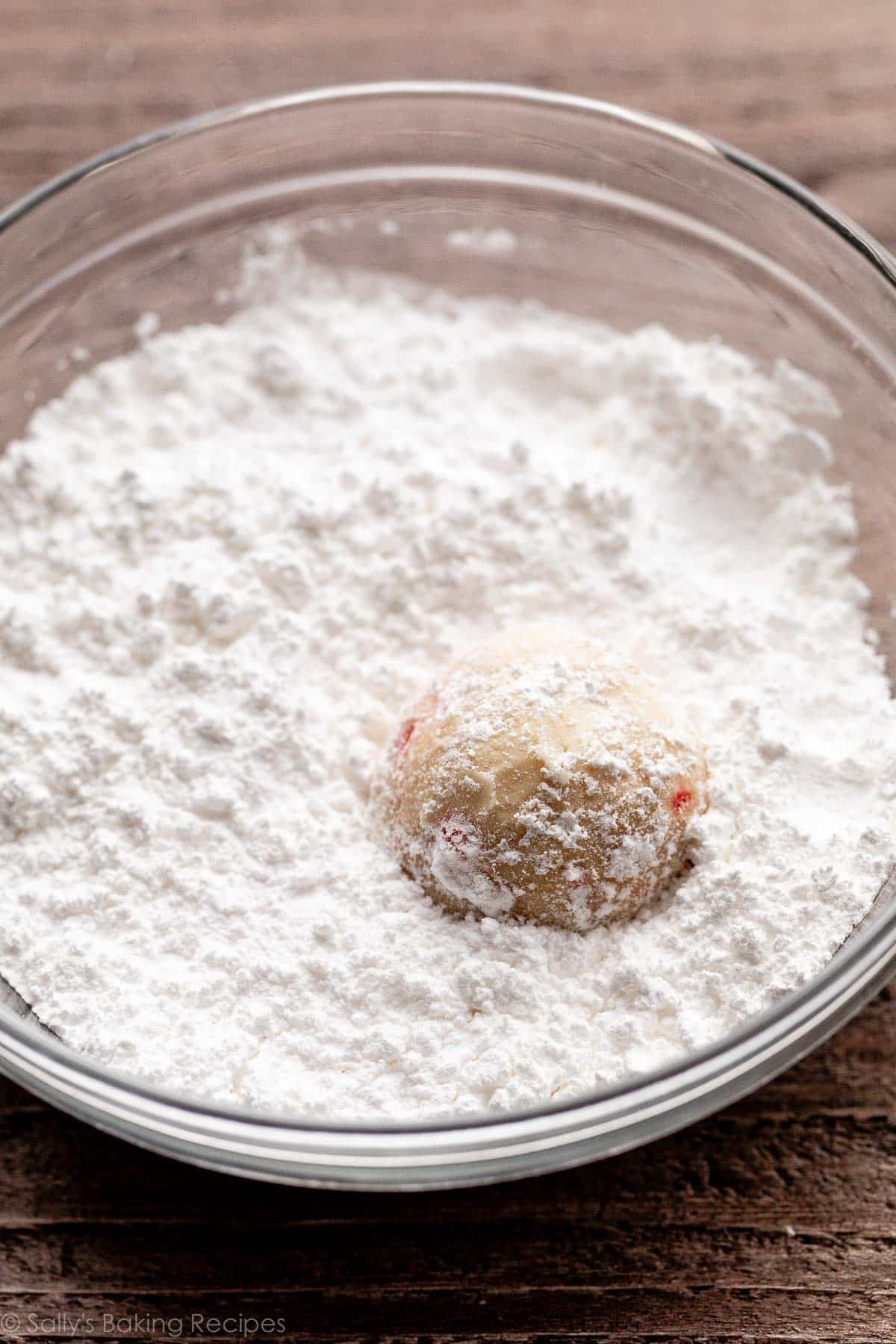 candy cane cookie in bowl of confectioners' sugar.