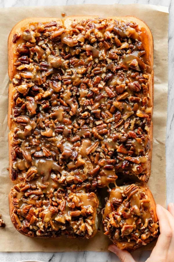 hand pulling a maple pecan sticky bun away from the batch.
