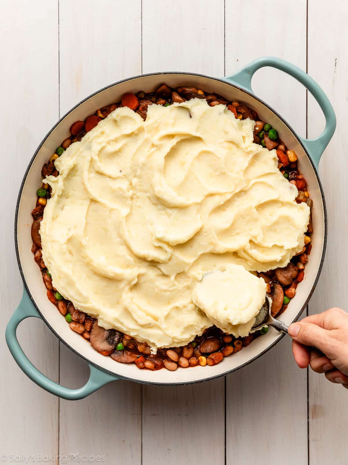 spreading mashed potatoes on bean and vegetable mixture.